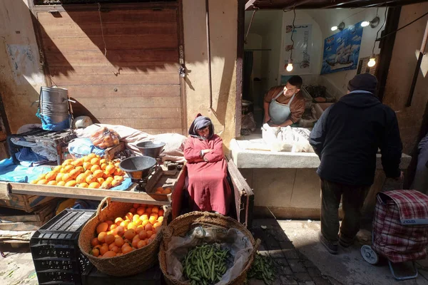 Old man selling fruits and vegetables in the roadside market Souk in the city of Fes in Morocco. Local shops on the road. A seafood shop next to a fruits shop. 