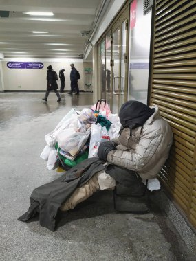 24.12.2021.Saint-Petersburg. - Rusya. Bir serseri, bir dilenci, elinde eşyasıyla evsiz bir adam kendini ısıtıyor ve kış ayazında metro geçidinde fan ızgarasında uyuyor.. 
