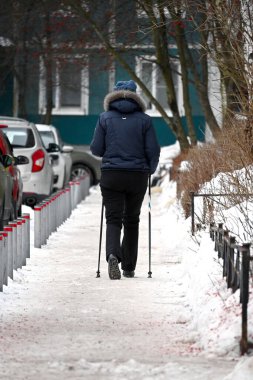 Kışın İskandinavya 'da bir kadın, çok katlı bir apartmanın avlusunda sopalarla tek başına yürüyor. Etkin bir yaşam tarzı. 