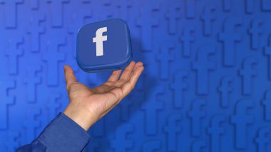Odaklanmamış mavi arka planda bir erkeğin eline düşen kare bir Facebook rozeti.