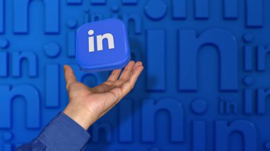 Odaklanmamış mavi arka planda bir erkeğin eline düşen kare bir Linkedin rozeti..