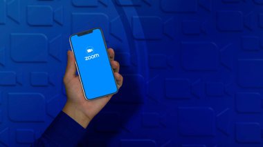 A male hand holds a smart phone with the Zoom logo on the screen.