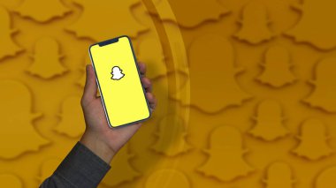 A male hand holds a smart phone with the Snapchat logo on the screen.