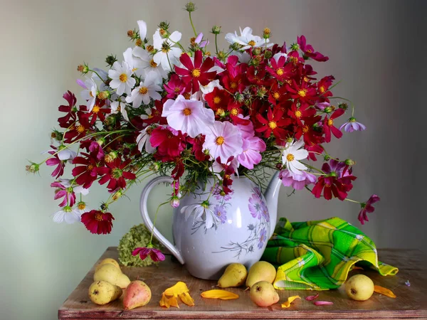 A beautiful bouquet with Cosmei in a vase with water and pears on the table.