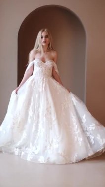 Zarif beyaz elbiseli genç sarışın kadın stüdyoda poz veriyor.