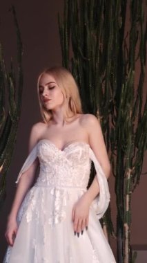 Zarif beyaz elbiseli genç sarışın kadın stüdyoda poz veriyor.