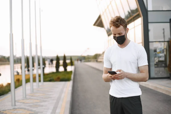 Portrait of a young fit man in a face mask jogging outdoors on a stadium