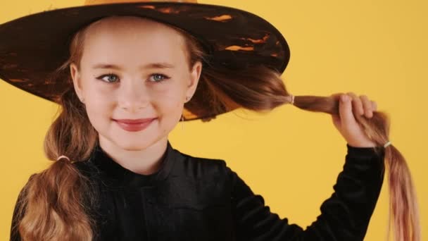 Cadılar Bayramı 'nda turuncu stüdyo arka planında cadı kostümlü küçük sarışın kız. — Stok video