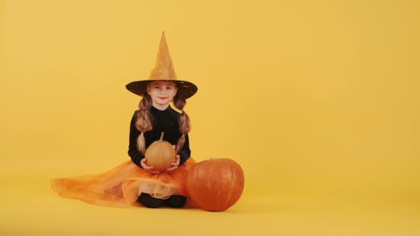 Niña rubia en traje de bruja en Halloween en fondo de estudio naranja — Vídeos de Stock