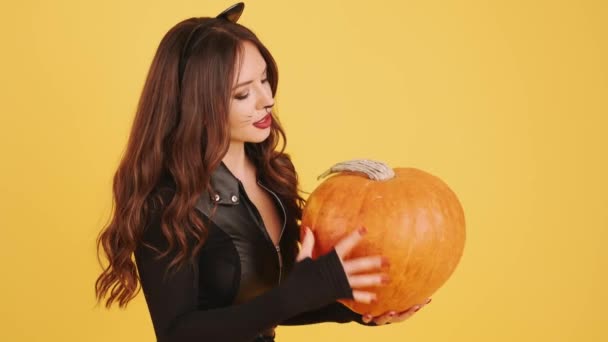 Женщина в макияже на Хэллоуин держит тыкву на оранжевом фоне — стоковое видео