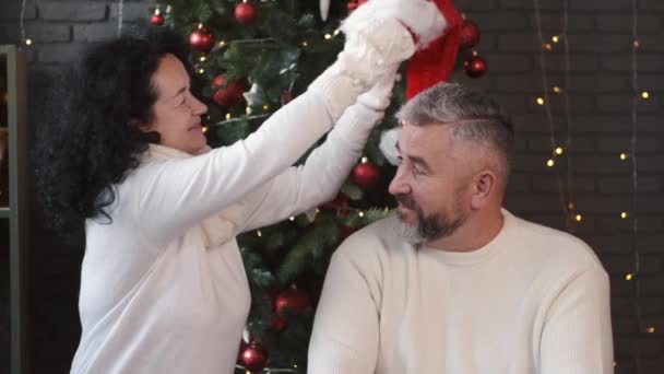 Mujer poniendo sombrero de santa en su marido guapo en Navidad — Vídeos de Stock