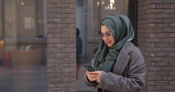 Muselman kvinna användande hennes telefon stående nära byggnad — Stockvideo
