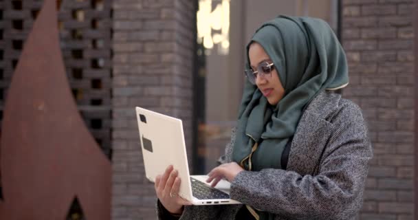 Femme musulmane utilisant ordinateur portable debout à l'extérieur — Video