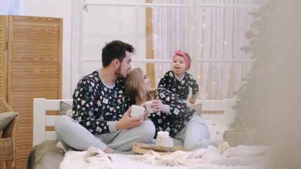 Sebuah keluarga muda dalam sweater hangat dengan seorang putri bayi di kamar tidur Natal — Stok Video