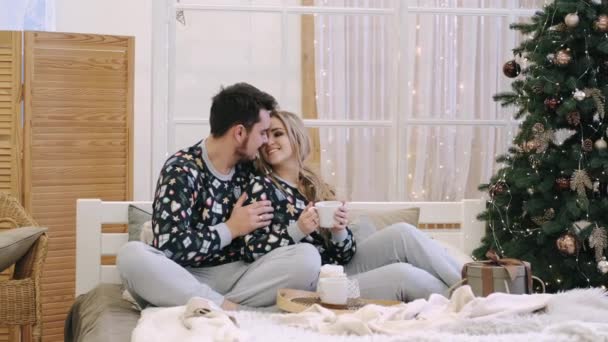 Aantrekkelijke vrolijke man en vrouw zitten in de buurt van kerstboom knuffelen — Stockvideo