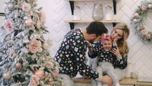 Eine junge Familie in warmen Pullovern mit einer kleinen Tochter im Weihnachtszimmer — Stockvideo
