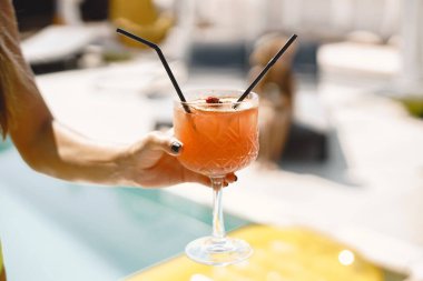 Havuz başında bir kadının elinde kokteyl.