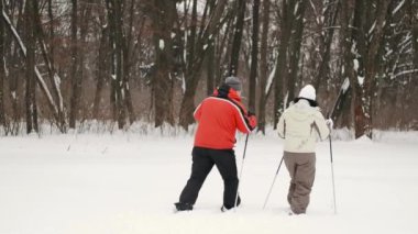 Üst düzey bir çift, ellerinde kayak sopalarıyla geziyor ve kışın ormanda doğanın tadını çıkarıyorlar.