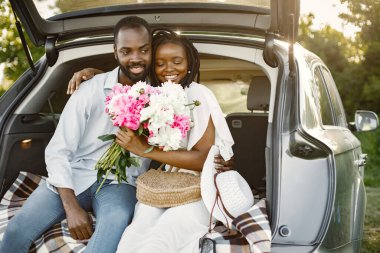 Parktaki genç mutlu çift arabanın bagajında oturuyor.