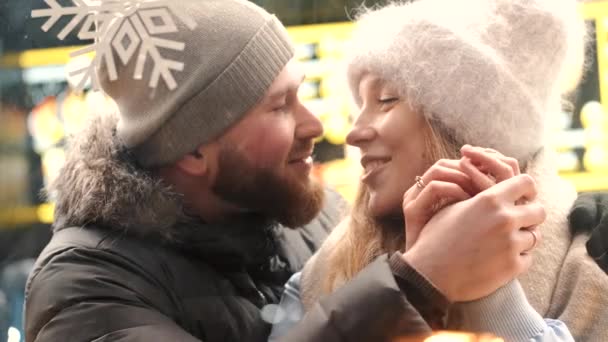 Um casal atraente apaixonado, um casal elegante vestindo roupas quentes abraçando e olhando uns aos outros na feira de inverno em um momento de Natal — Vídeo de Stock