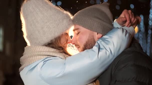 Una atractiva pareja enamorada, una elegante pareja con ropa abrigada abrazándose y mirándose en la feria de invierno en Navidad — Vídeo de stock