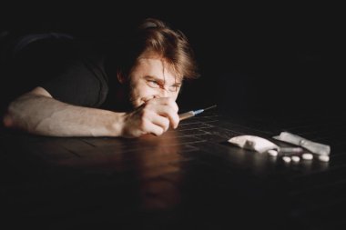 Keş adam şırıngaya uzanıyor.