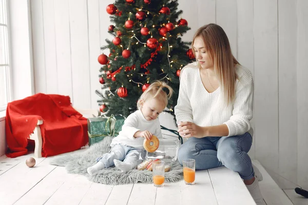 Madre con la pequeña hija sentada cerca del árbol de Navidad e ir donuts. — Foto de Stock