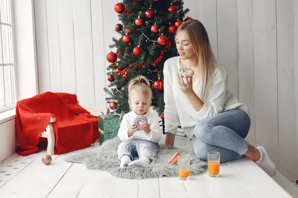 Madre con la pequeña hija sentada cerca del árbol de Navidad e ir donuts. — Foto de Stock