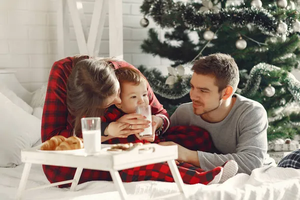 Hermosa familia sentada en la cama abrazando y comiendo galletas — Foto de Stock