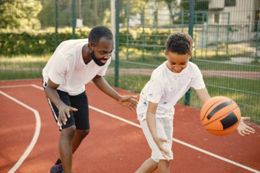 Siyah baba ve oğlu basketbol sahasında birlikte oynuyorlar.