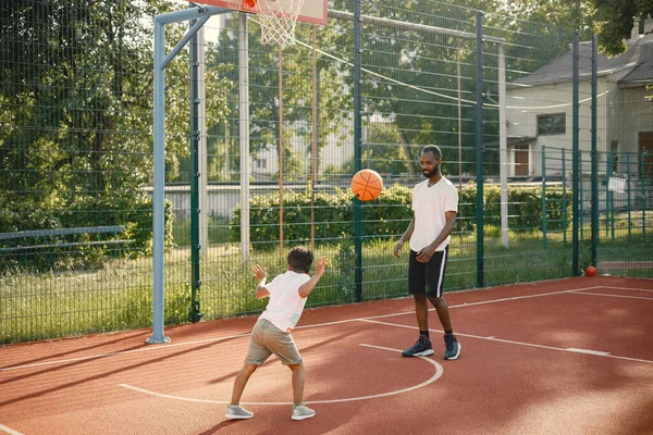 Pai negro com filho jogando basquete na quadra de basquete juntos — Fotografia de Stock