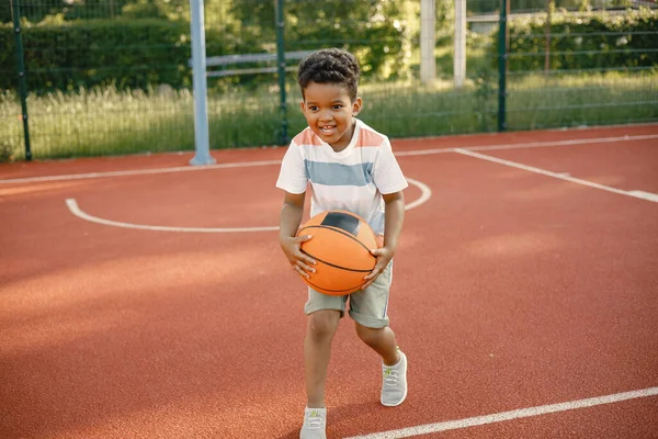 Rapaz multirracial de pé em um campo de basquete e jogar com uma bola laranja — Fotografia de Stock