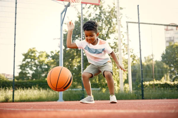 Rapaz multirracial de pé em um campo de basquete e jogar com uma bola laranja — Fotografia de Stock