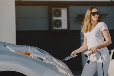 Elektrikli benzin istasyonunda kadın elektro arabayı şarj ediyor.