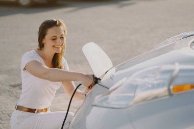 Elektrikli benzin istasyonunda kadın elektro arabayı şarj ediyor.