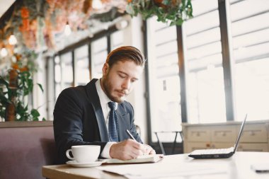 Kafede dizüstü bilgisayarlı bir adam oturuyor.