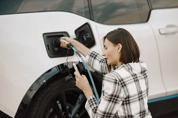 Businesswoman on the electric cars charge station using a phone — Stock Photo, Image