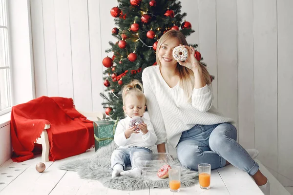 Madre con la pequeña hija sentada cerca del árbol de Navidad e ir donuts. — Foto de Stock