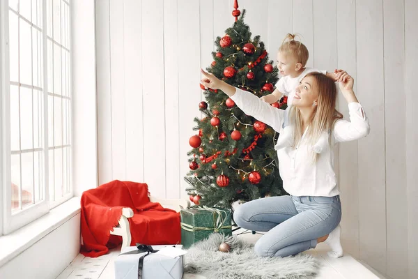 Madre con hija pequeña sentada junto al árbol de Navidad y divirtiéndose. — Foto de Stock