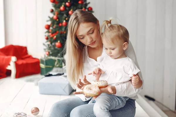 Madre con la pequeña hija sentada cerca del árbol de Navidad e ir donuts. — Foto de Stock