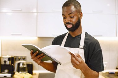 Afro-Amerikalı bir adam mutfakta yemek kitabı okuyor.