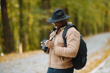 Siyah bir adam yolda duruyor ve elinde profesyonel bir kamera tutuyor.