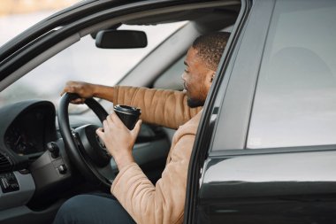 Arabasında oturup kahve içen ciddi bir siyahi adamın portresi.