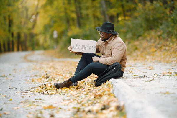 Homem negro carona em uma estrada e segurando um sinal em qualquer lugar — Fotografia de Stock