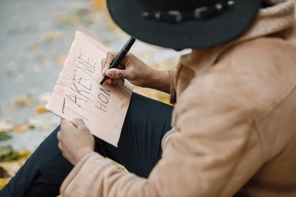 Černoch sedí na silnici a píše ceduli pro autostop — Stock fotografie