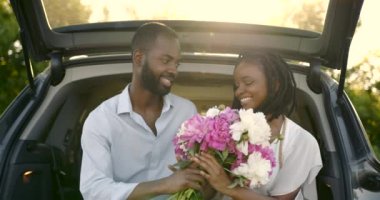 Parktaki genç mutlu çift arabanın bagajında oturuyor.