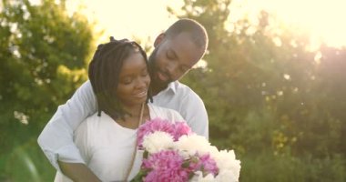 Black romantic couple with peony bunch in rural setting
