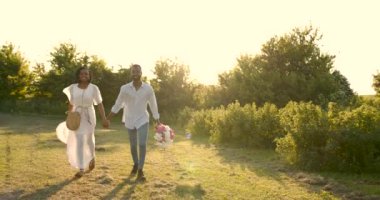 Black newlyweds walking with bouquet in nature