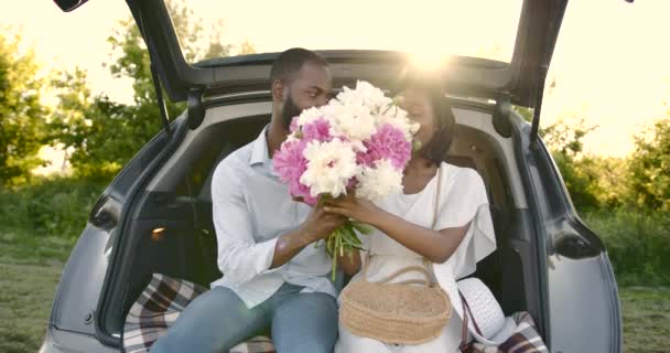 Jeune couple heureux dans un parc assis dans le coffre de la voiture — Video