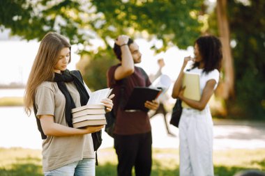 Three international students standing in a park and holding a books